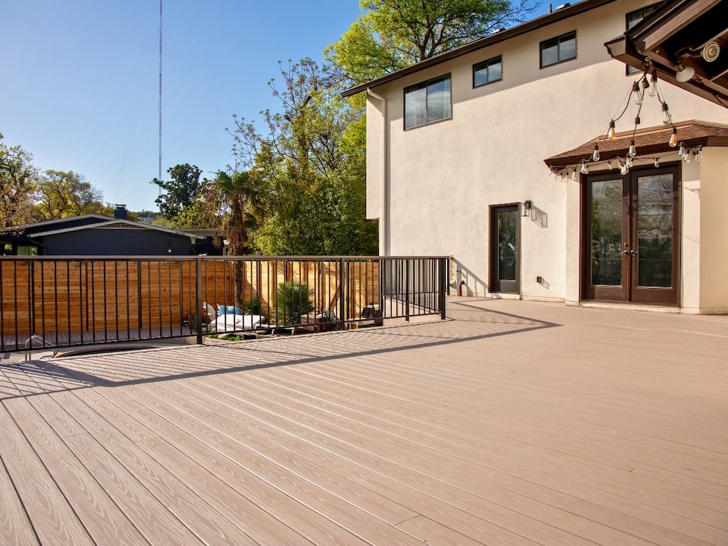 spacious backyard deck with wooden flooring and metal railing under clear blue sky. Adjacent to a modern house with large windows and patio doors.
